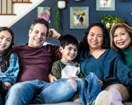 A family of 5 sits on a couch and smiles at the camera.