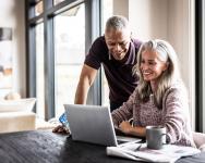 A middle-aged couple looking at a laptop on a desk at home.